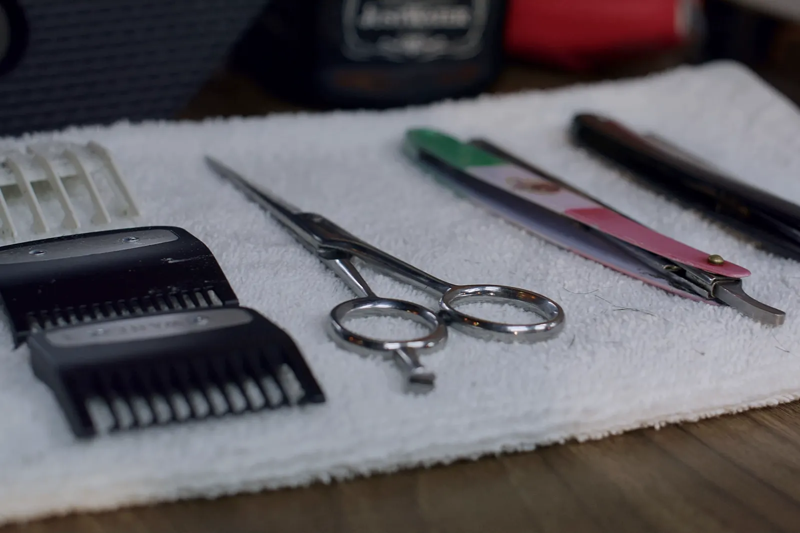 Clipper guards, shears and a razor laid out on a white towel